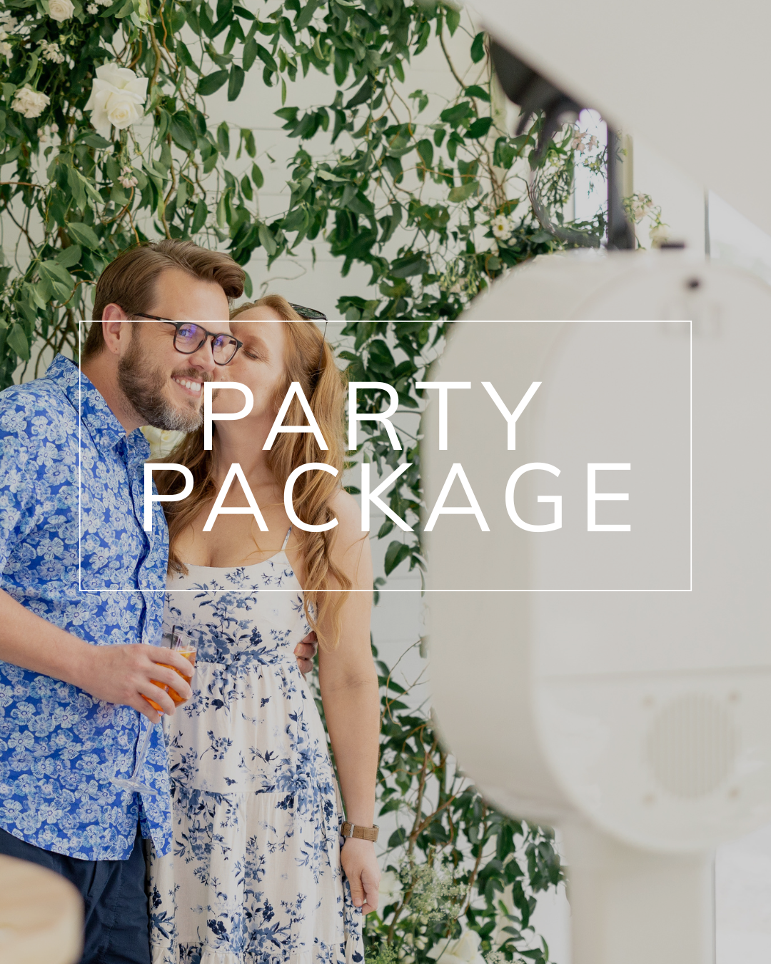 A man and woman standing together in front of greenery and a photo booth, with the words