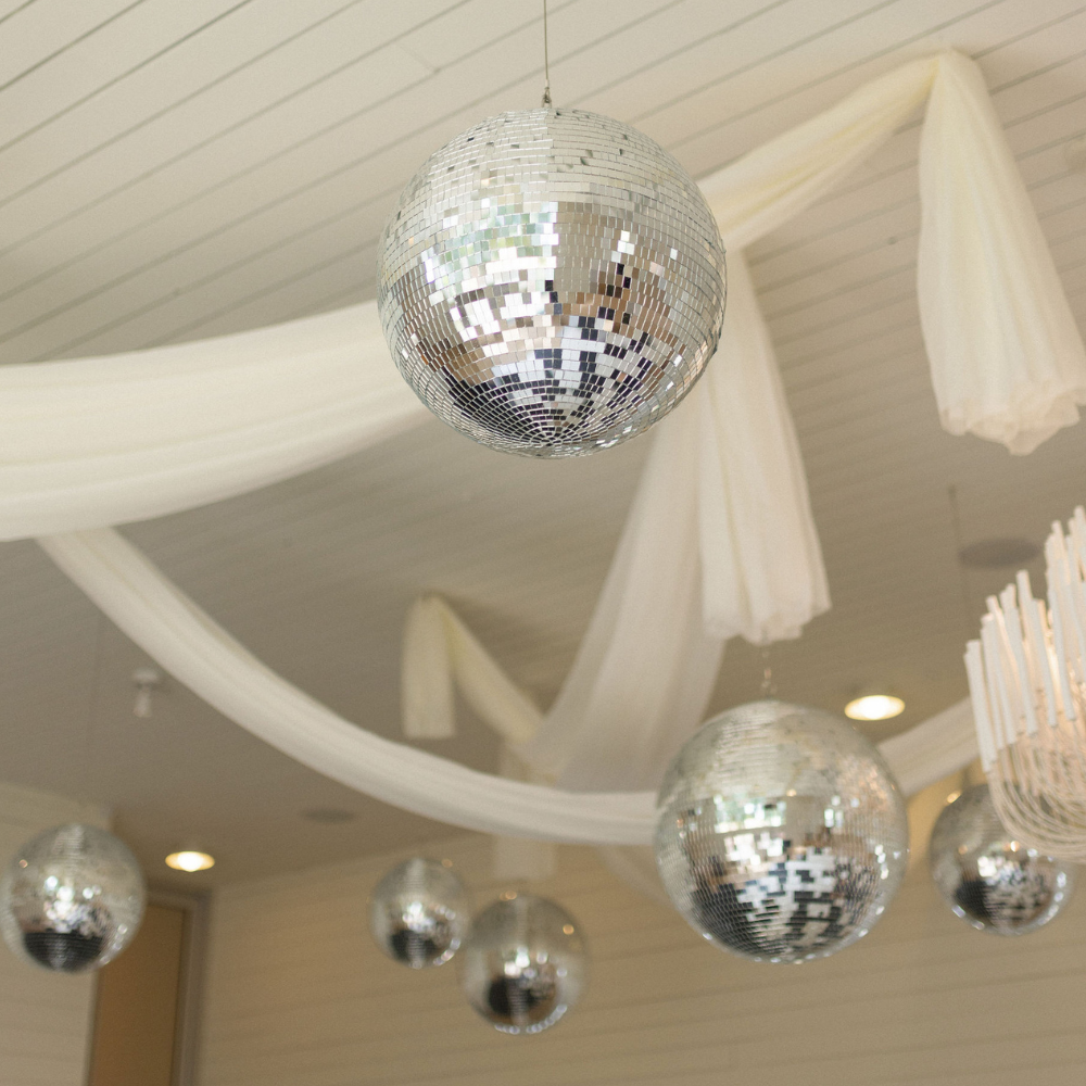 Disco balls and white draped fabric hanging from a ceiling in a decorated indoor venue