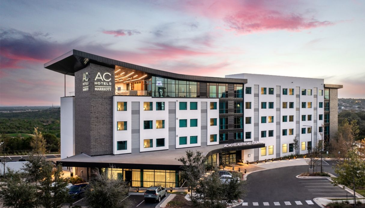 An aerial view of an AC Hotel building with a lot of windows and a large parking lot.