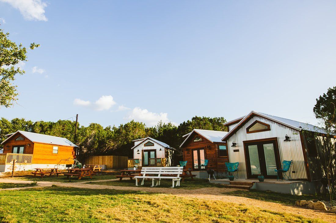 A group of small houses are sitting on top of a lush green field with picnic tables in front of the homes. 