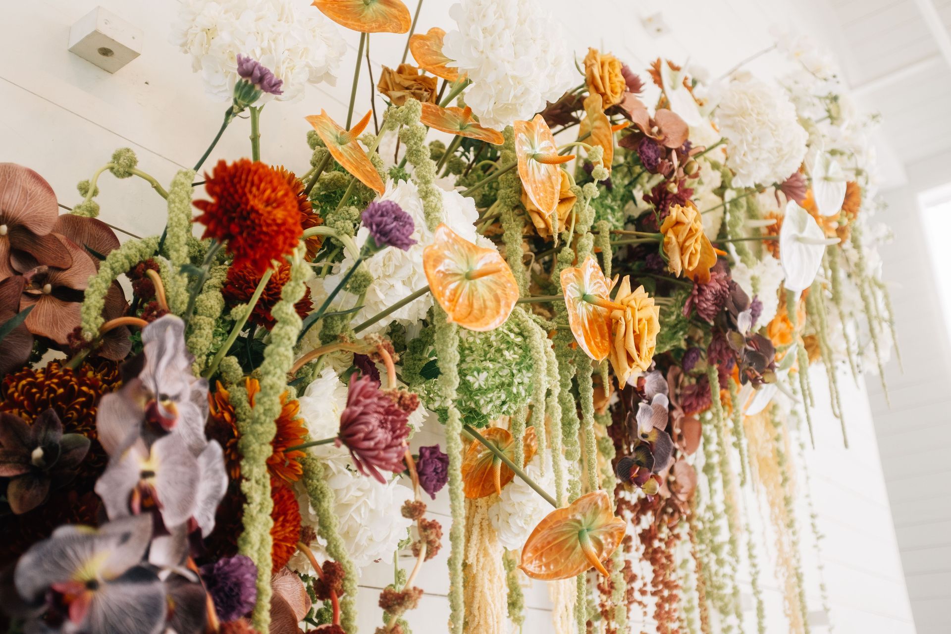 A lush, hanging floral arrangement in shades of orange, deep purple, and white, with cascading green textures.