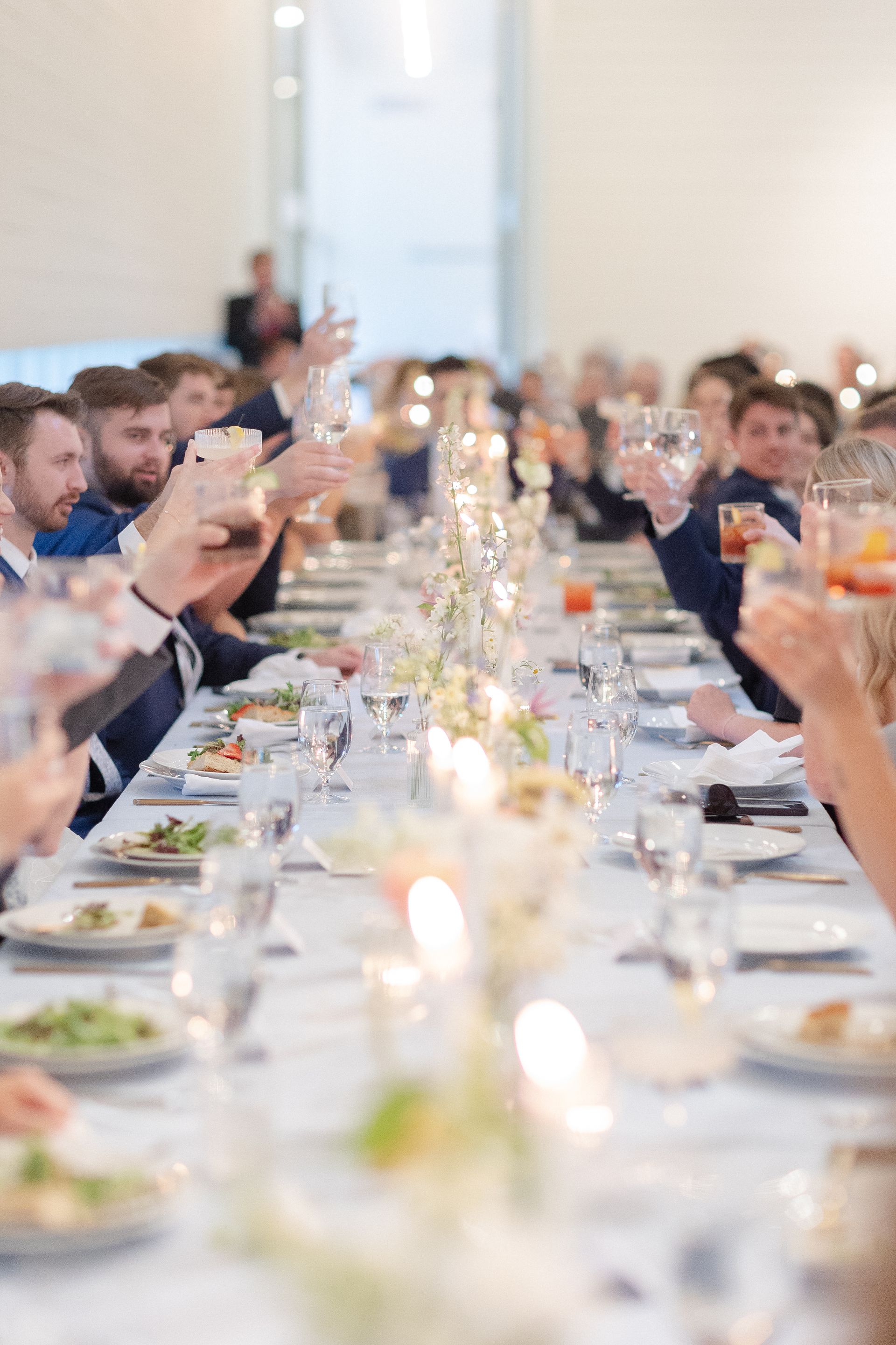 A group of people are sitting at a long table toasting with wine glasses.