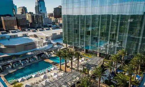 An aerial view of a full window building with a swimming pool and palm trees in front of it.