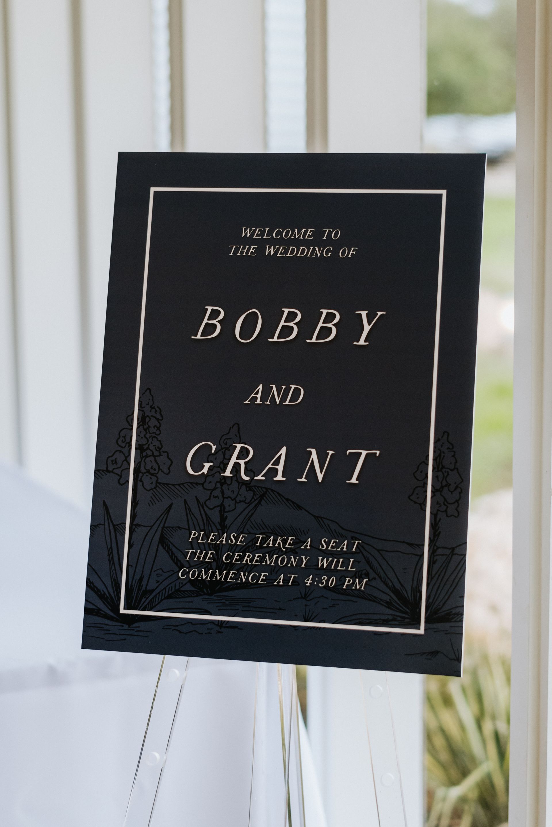 A black wedding welcome sign on an easel with gold text reading, 