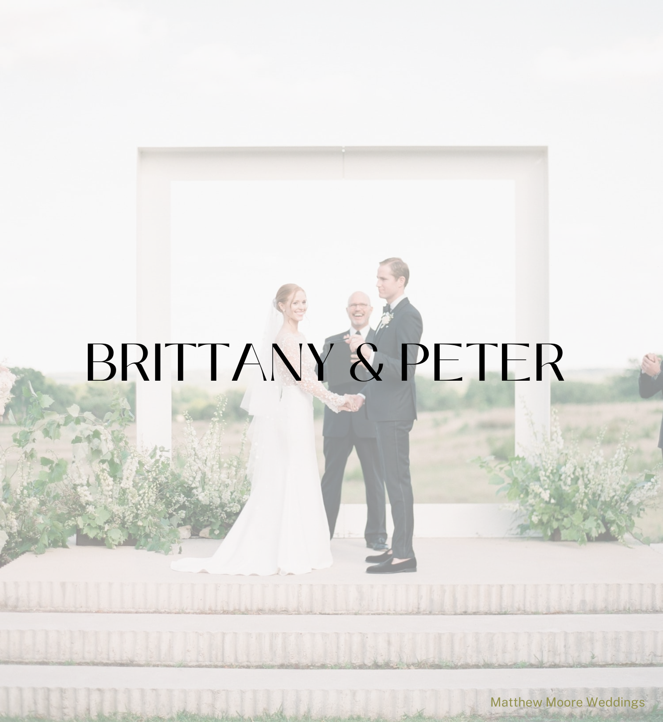 A couple stands holding hands before an officiant in front of a white frame arch at an outdoor wedding ceremony.