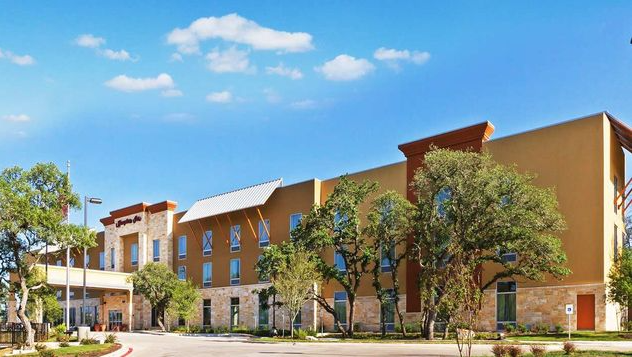 A large Hampton Inn hotel with a lot of windows and trees in front of it.