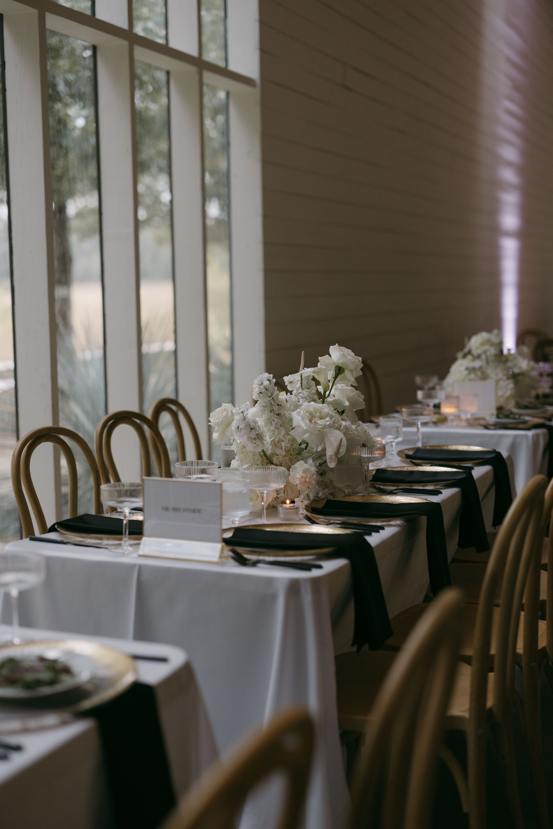 A long table set for dinner with white tables and black napkins and champagne flutes.
