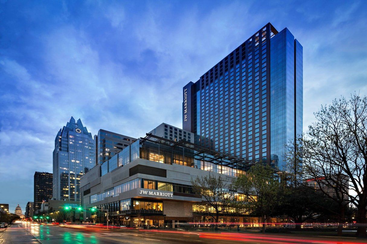 A sleek all glass building with a lot of windows is in the middle of a city.