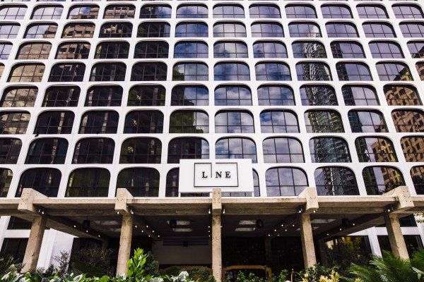 A building with arched windows that are consistently around and the same size with a sign that says the hotel's name on it: Line Hotel. 