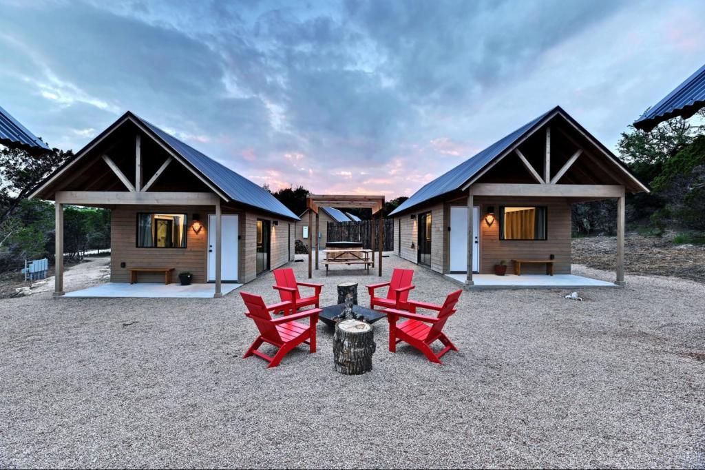 A group of cabin like houses with red chairs and a fire pit in front of them