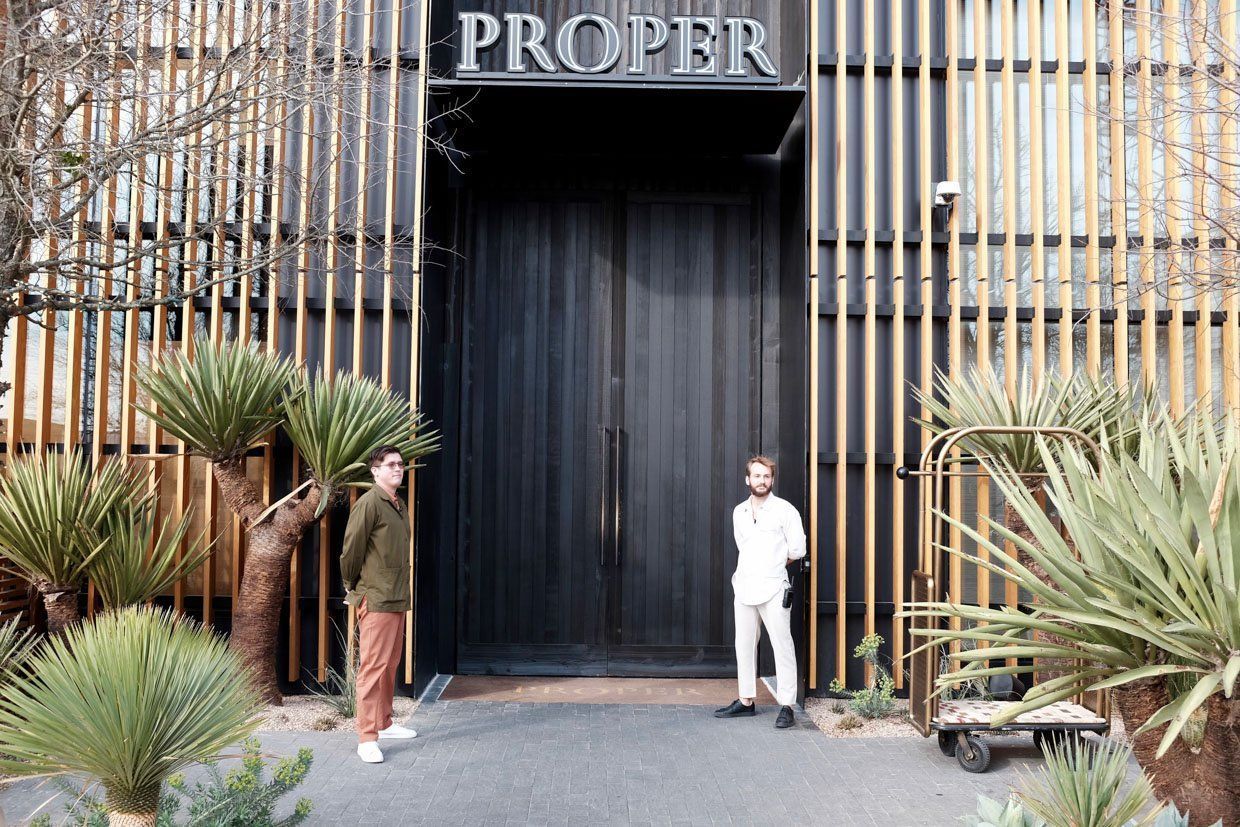Proper Hotel is a boutique hotel in downtown Austin. Two men are standing at the front entrance to the hotel with a large black door. 