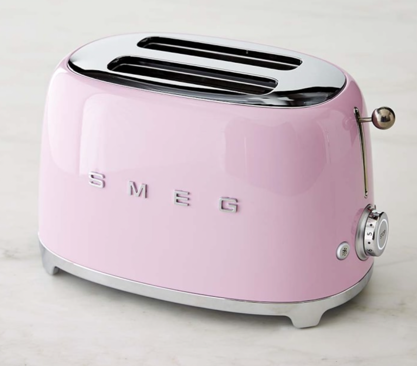 A pastel pink Smeg two-slice toaster with a chrome top and base, sitting on a light-colored surface.