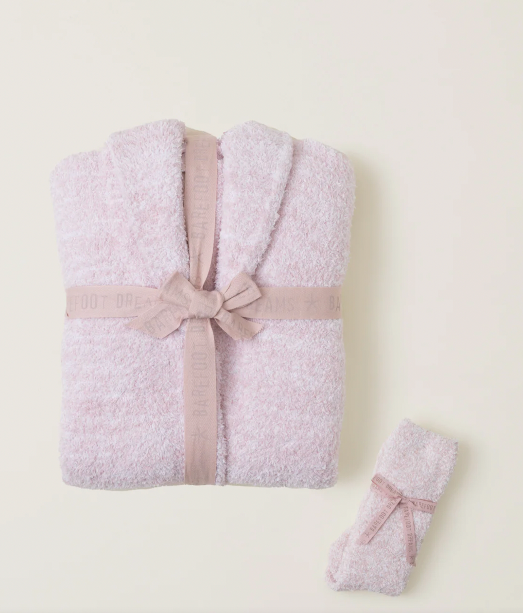 A folded lavender, fuzzy bathrobe and matching socks tied with a mauve ribbon against a plain cream background.