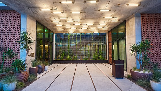 A large entrance to a hotel with a lot of windows and plants in front of it.
