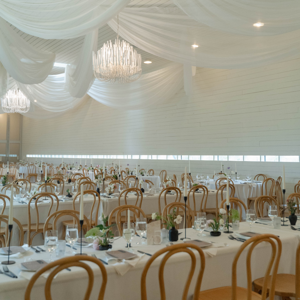 Outdoor wedding ceremony setting with rows of wooden chairs, a stone aisle, and a floral-decorated arch against a field.