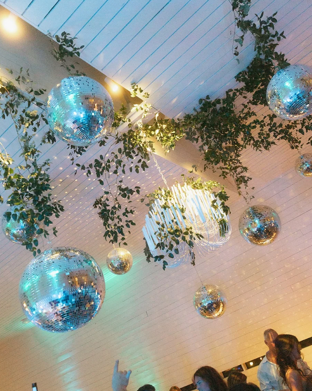 Reflective disco balls and hanging greenery on a white ceiling in a warmly lit event space