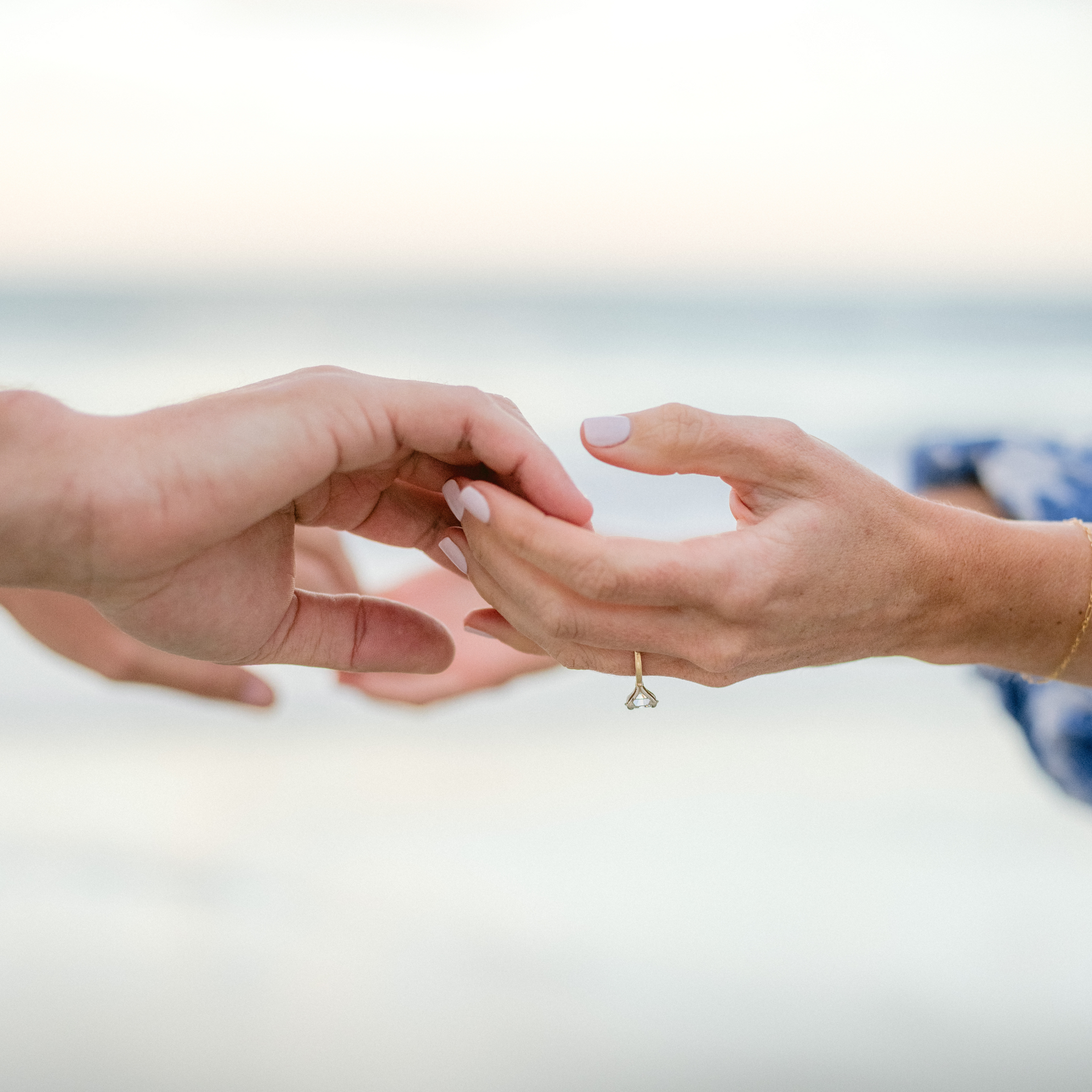 Two hands reach toward each other in a gentle, caring gesture against a soft, blurred beach background.