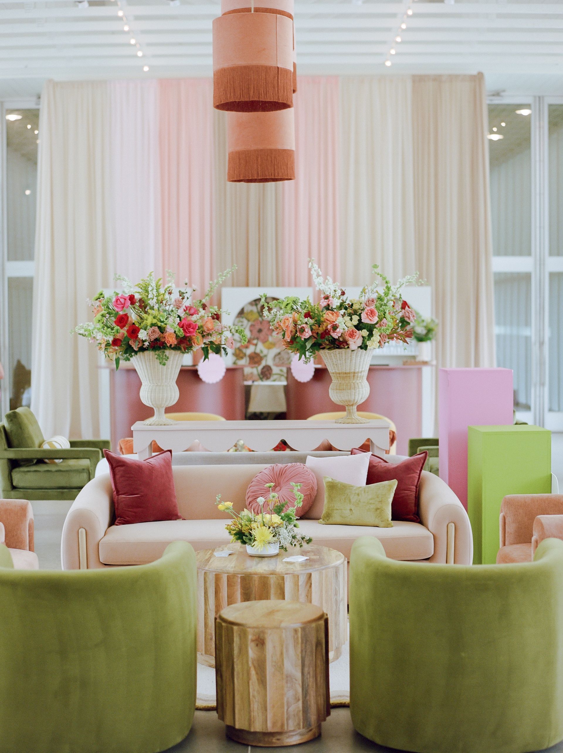 A stylish lounge area with a blush sofa, two olive green chairs, floral centerpieces, and a tiered copper light fixture.