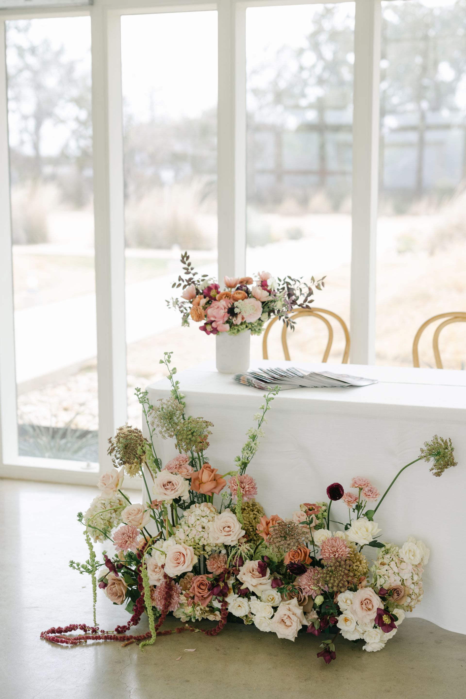A white table with a floral centerpiece and a lush arrangement of blush, peach, and cream flowers at its base.