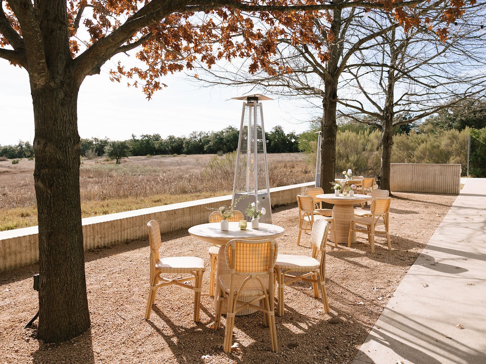 Outdoor patio area at Prospect House with round tables, chairs, and a tall metal heater on gravel under trees, overlooking the Hill Country.