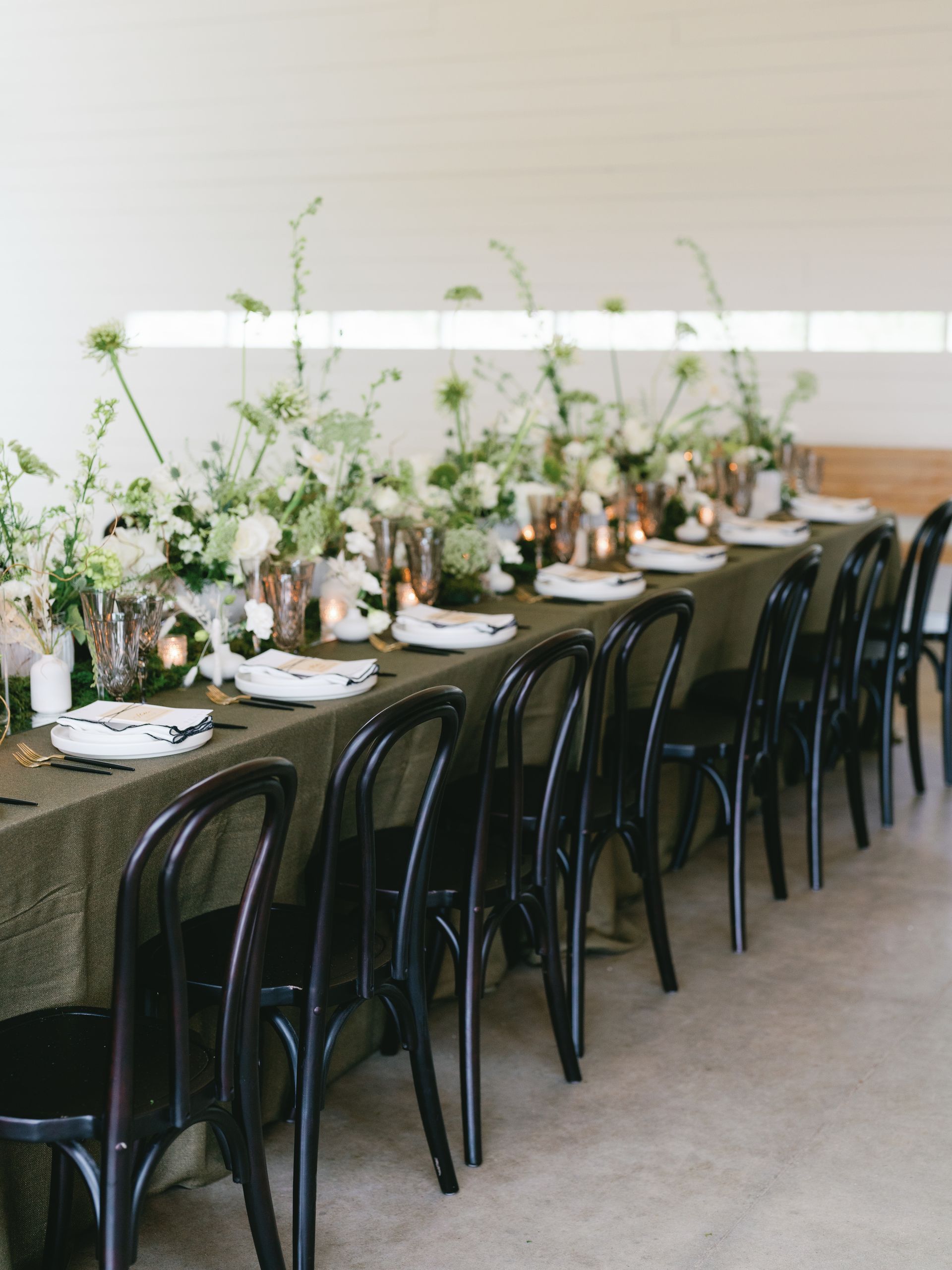 A long table with black chairs and green and white flowers on it.
