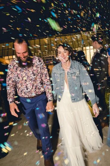 A couple walks hand-in-hand outdoors while bubbles falls around them, both laughing joyfully leaving Prospect House.