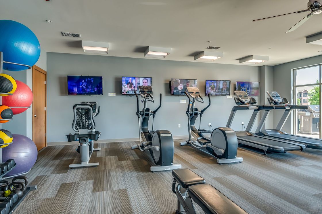 Wooden deck with white cushioned bench and small table, surrounded by lush green trees.