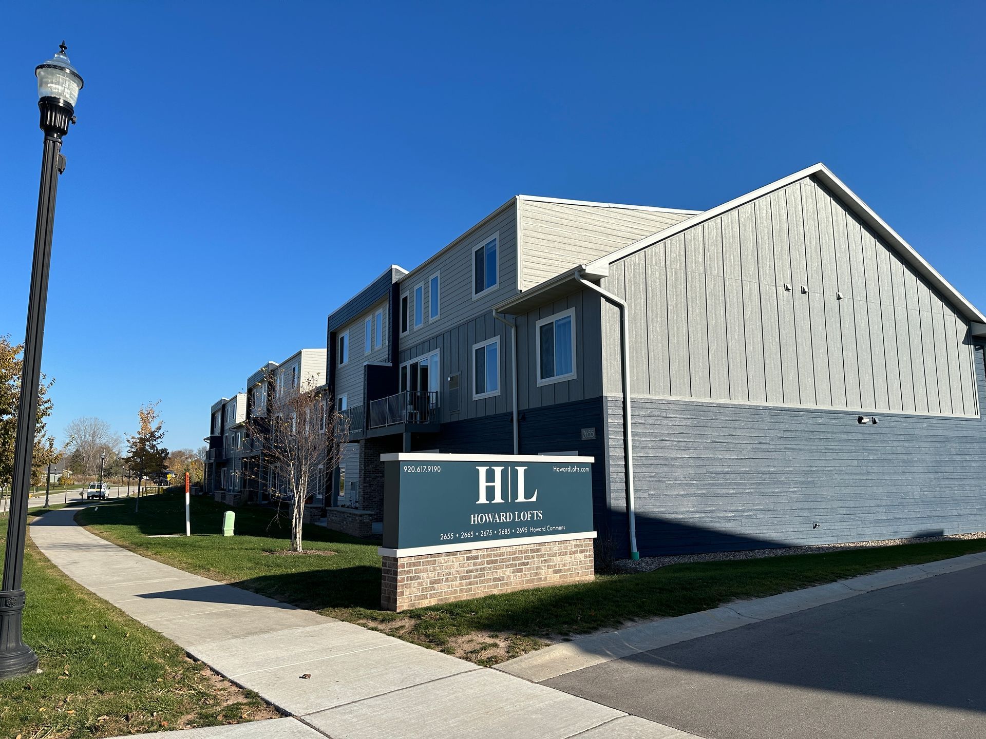 Modern apartment complex with gray siding, sidewalk, and a sign in front on a sunny day