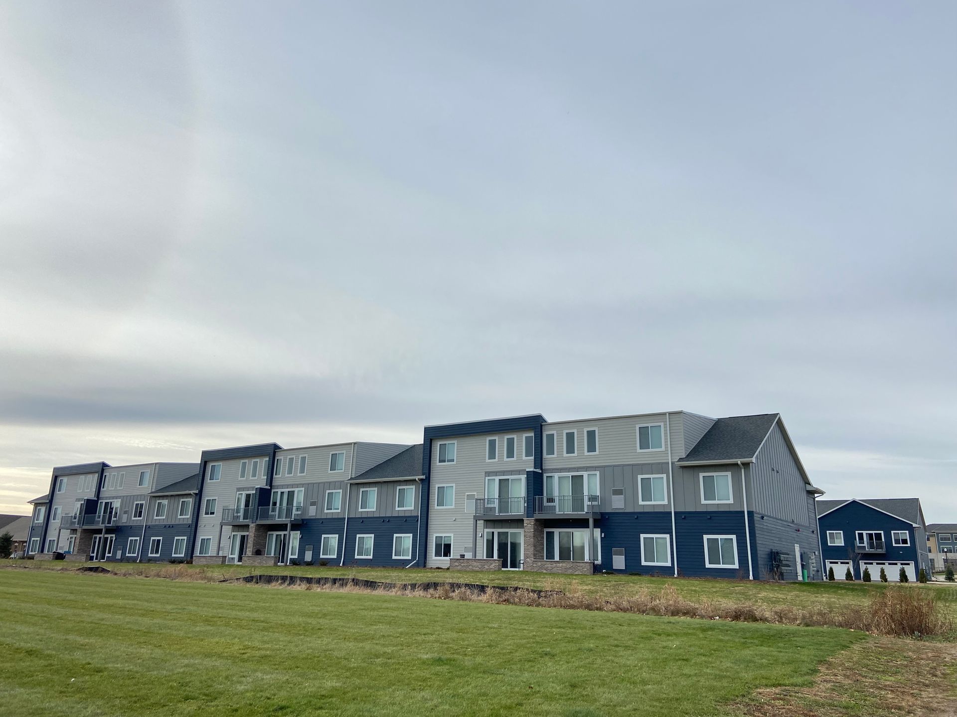 Row of modern waterfront houses beside a grassy field under a cloudy sky
