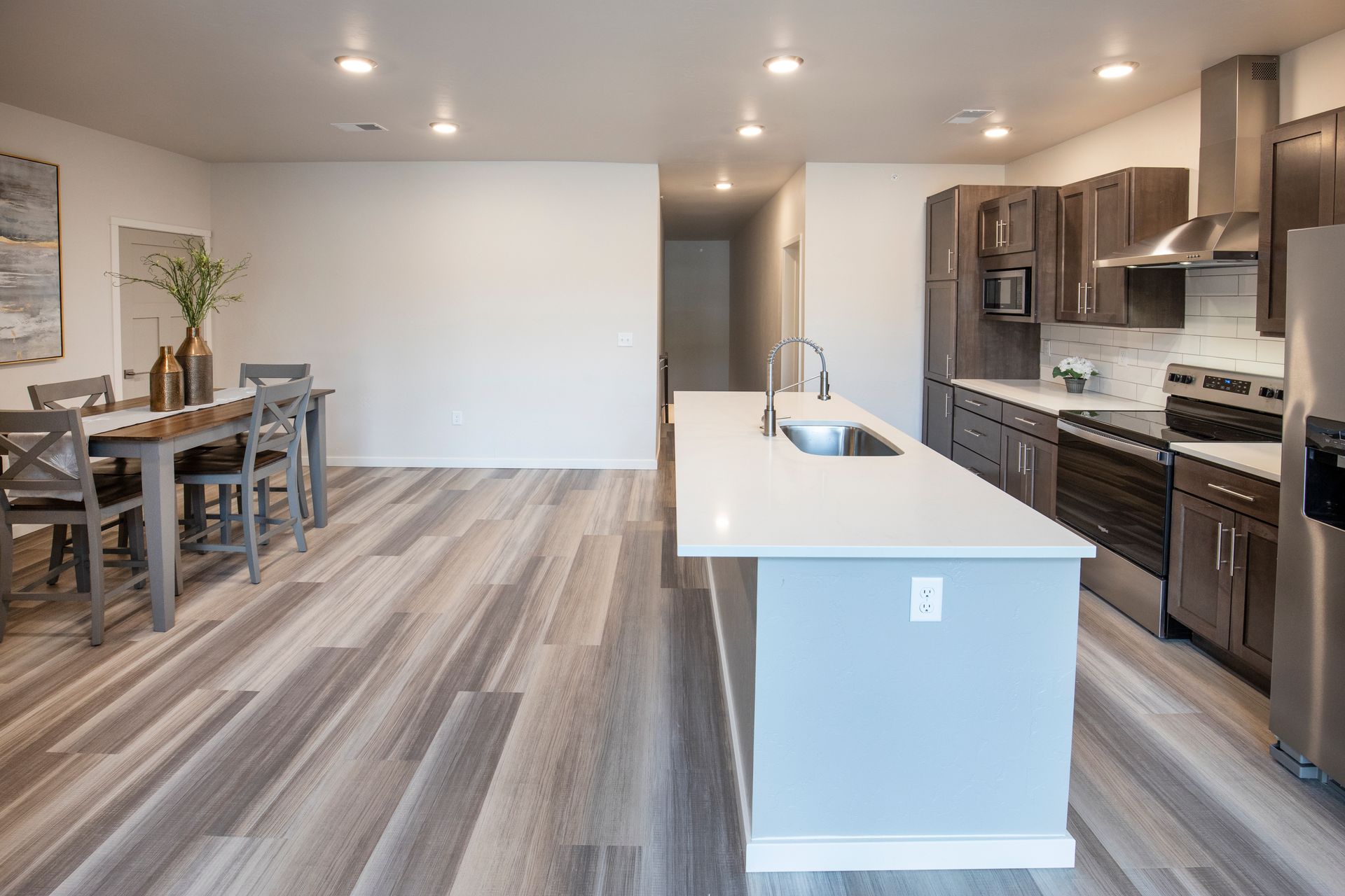 Modern open-concept kitchen and dining area with white island, dark cabinets, and wood-look flooring