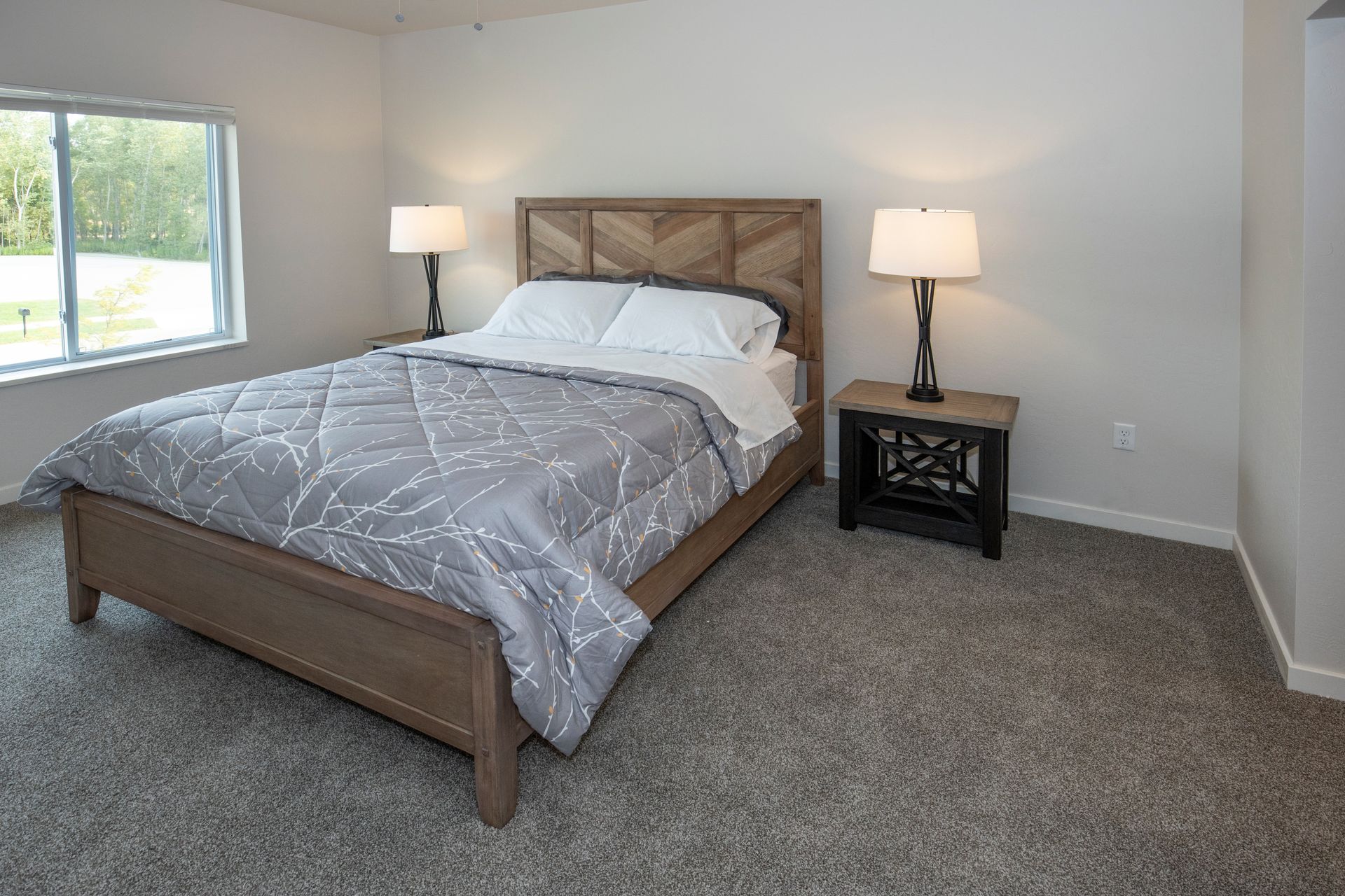 Bedroom with a gray bedspread, two bedside lamps, and a window on the left