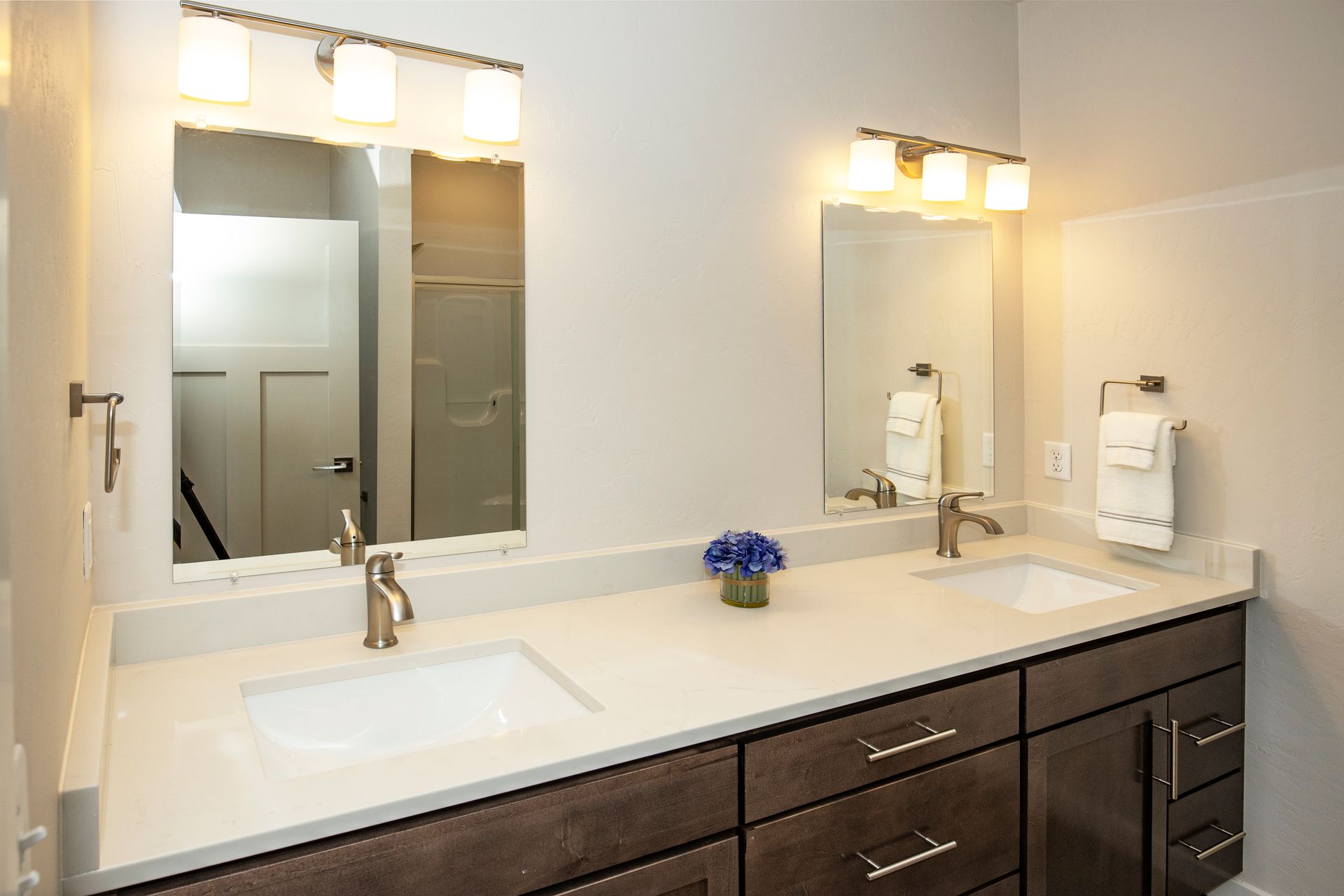 Bright bathroom vanity with double mirrors, white countertop, and dark wood cabinets.