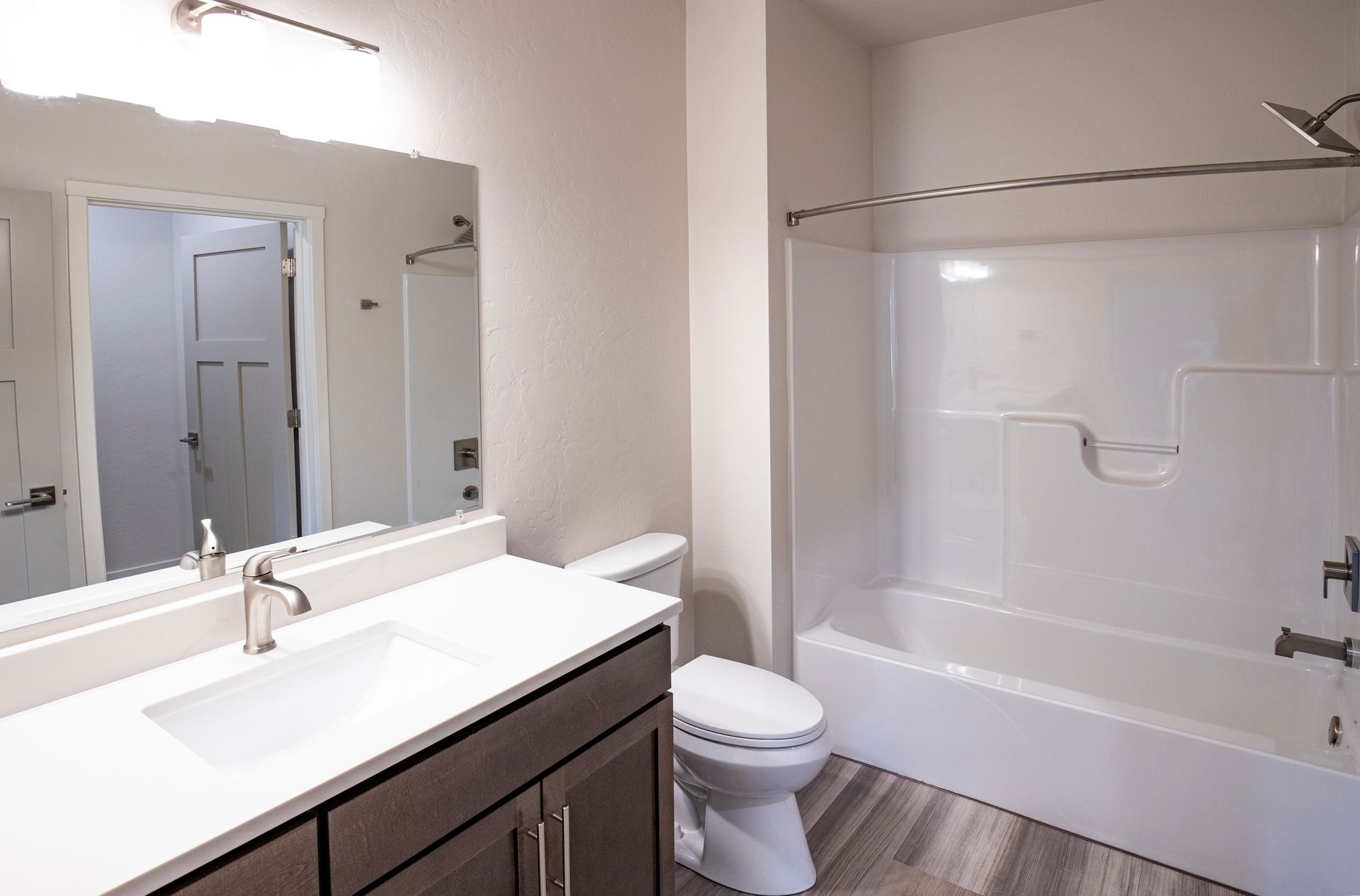 Modern bathroom with white tub, dark vanity, large mirror, and light wood-look floor.