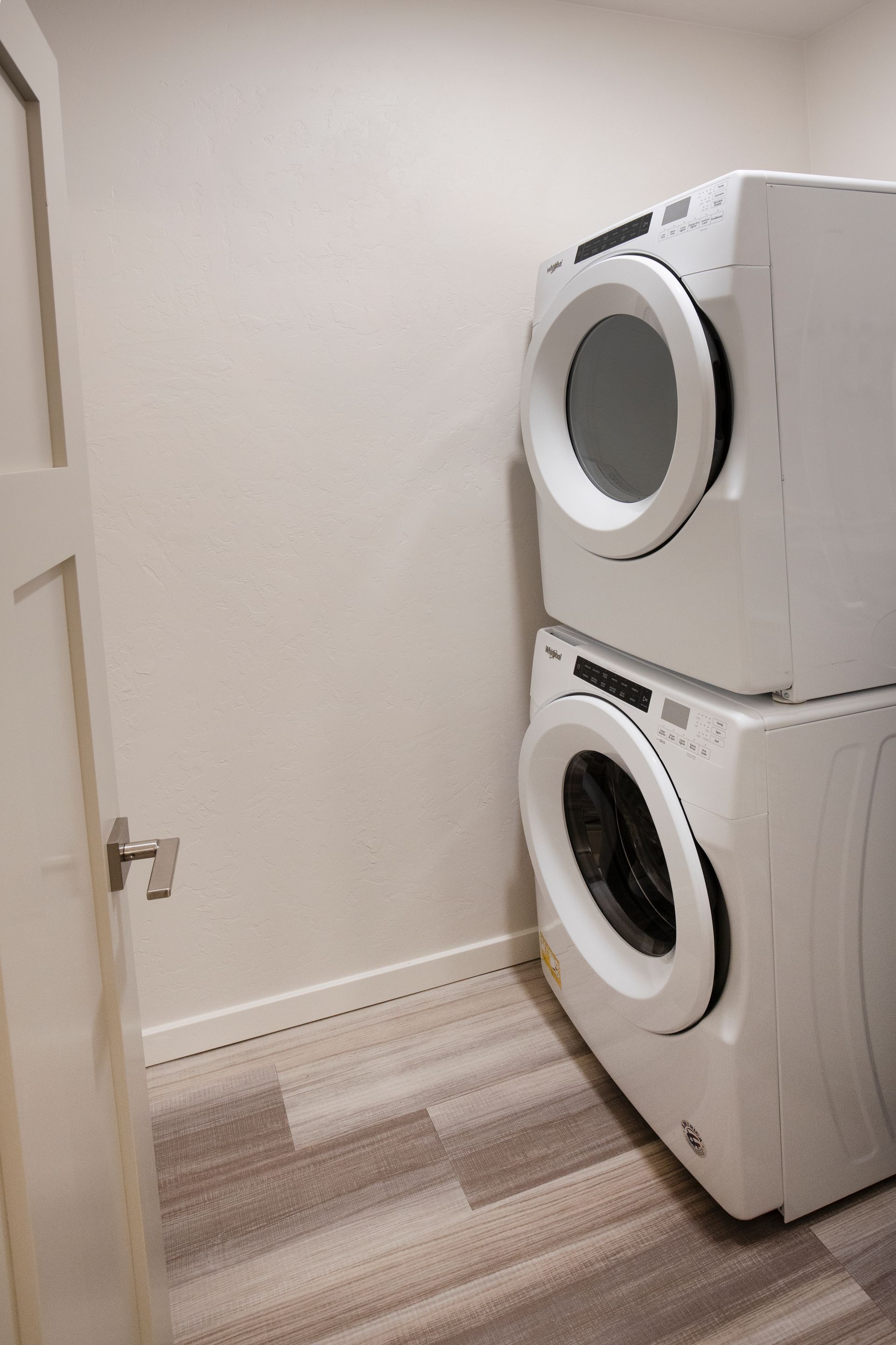 Laundry closet with stacked white washer and dryer on a beige floor in a narrow room