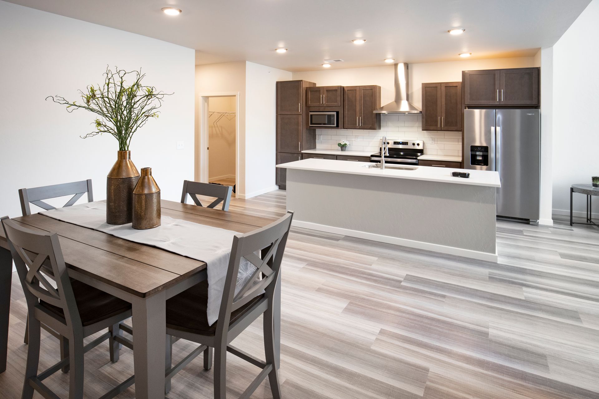 Modern dining and kitchen area with gray table, dark chairs, white cabinets, and stainless steel appliances