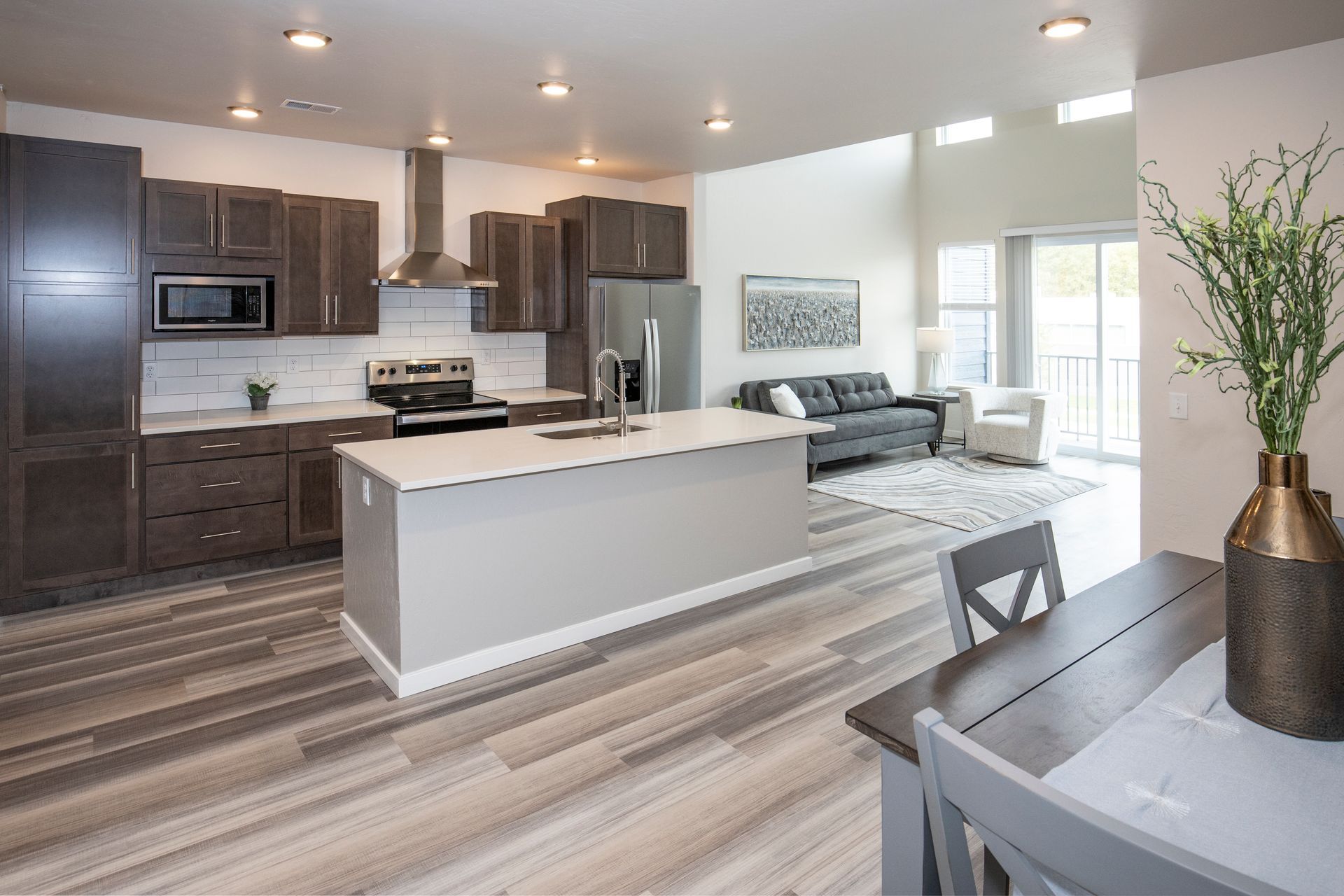 Bright open-concept kitchen and dining area with gray cabinetry, white island, and striped wood floors.