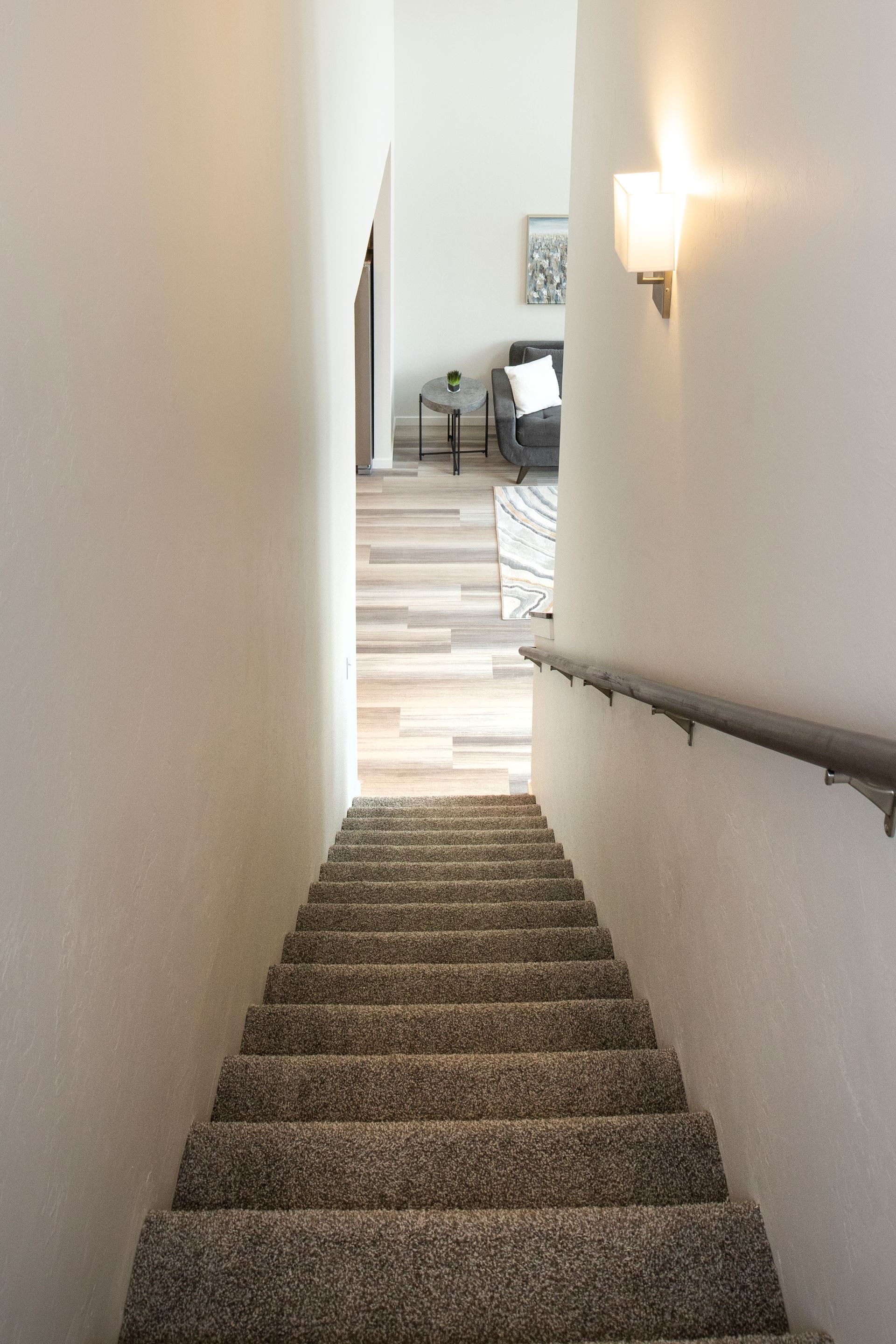 Narrow carpeted staircase leading to a bright hallway with a wall light and handrail
