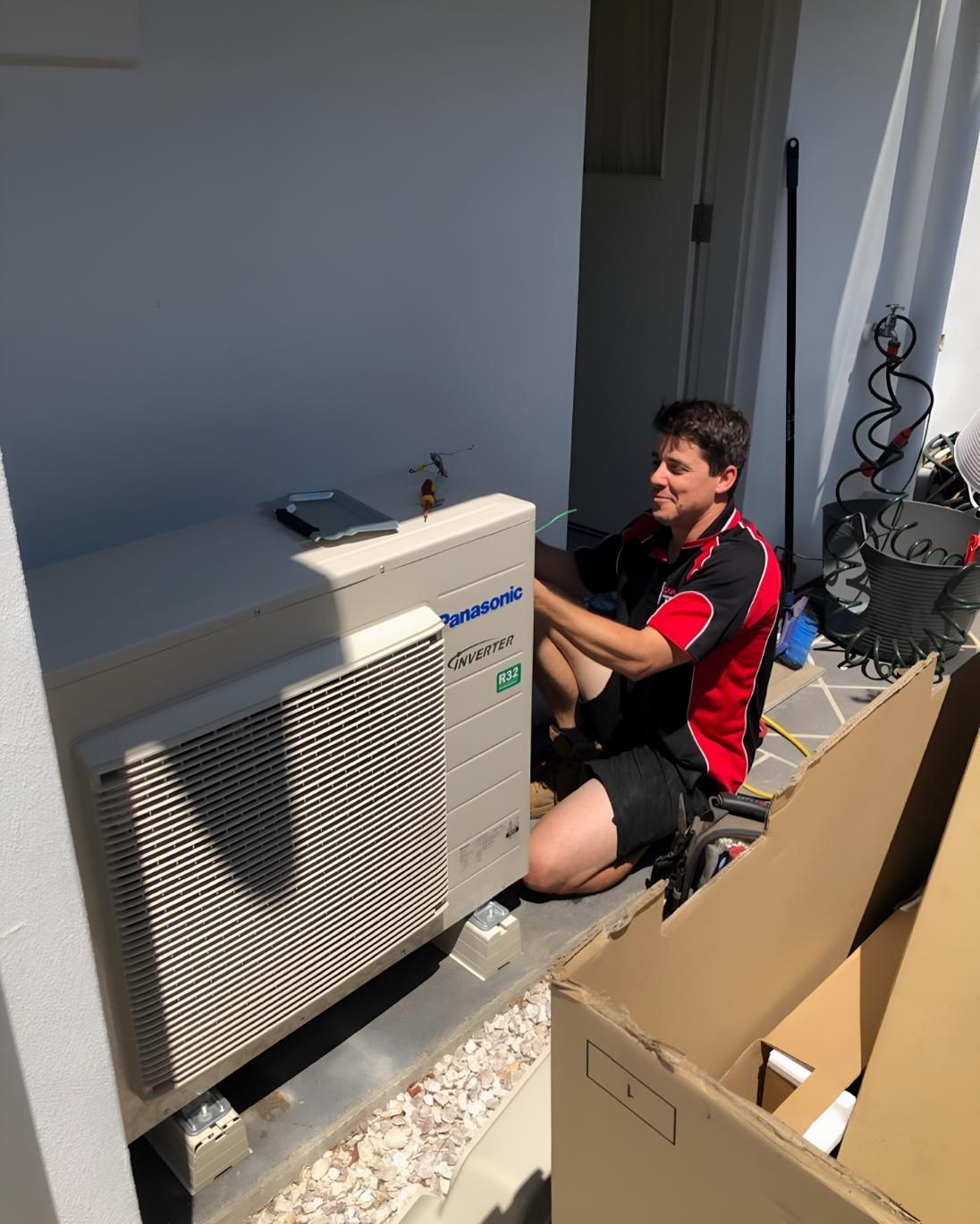 A man on his knees fixing an outdoor air conditioning unit - air conditioning lismore
