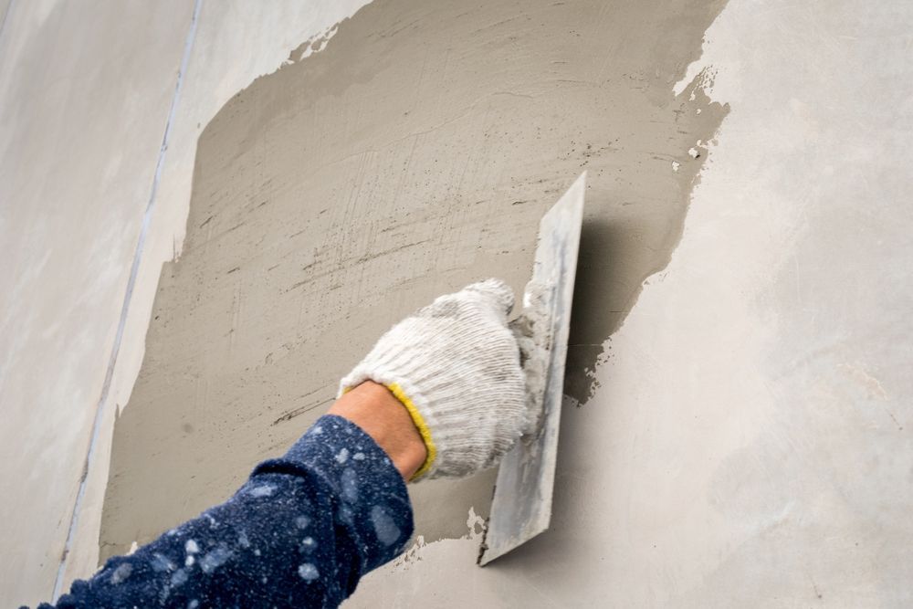 Person with Gloved Hand Using a Trowel to Apply Plaster to A Wall — Completely Plastered North Coast in Mullumbimby, NSW