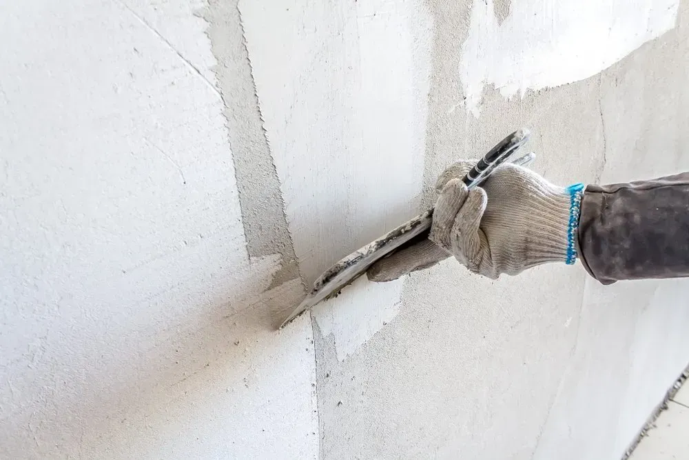 A Person Wearing a Glove Smooths Fresh Plaster on A Wall with A Trowel — Completely Plastered North Coast in Goonellabah, NSW