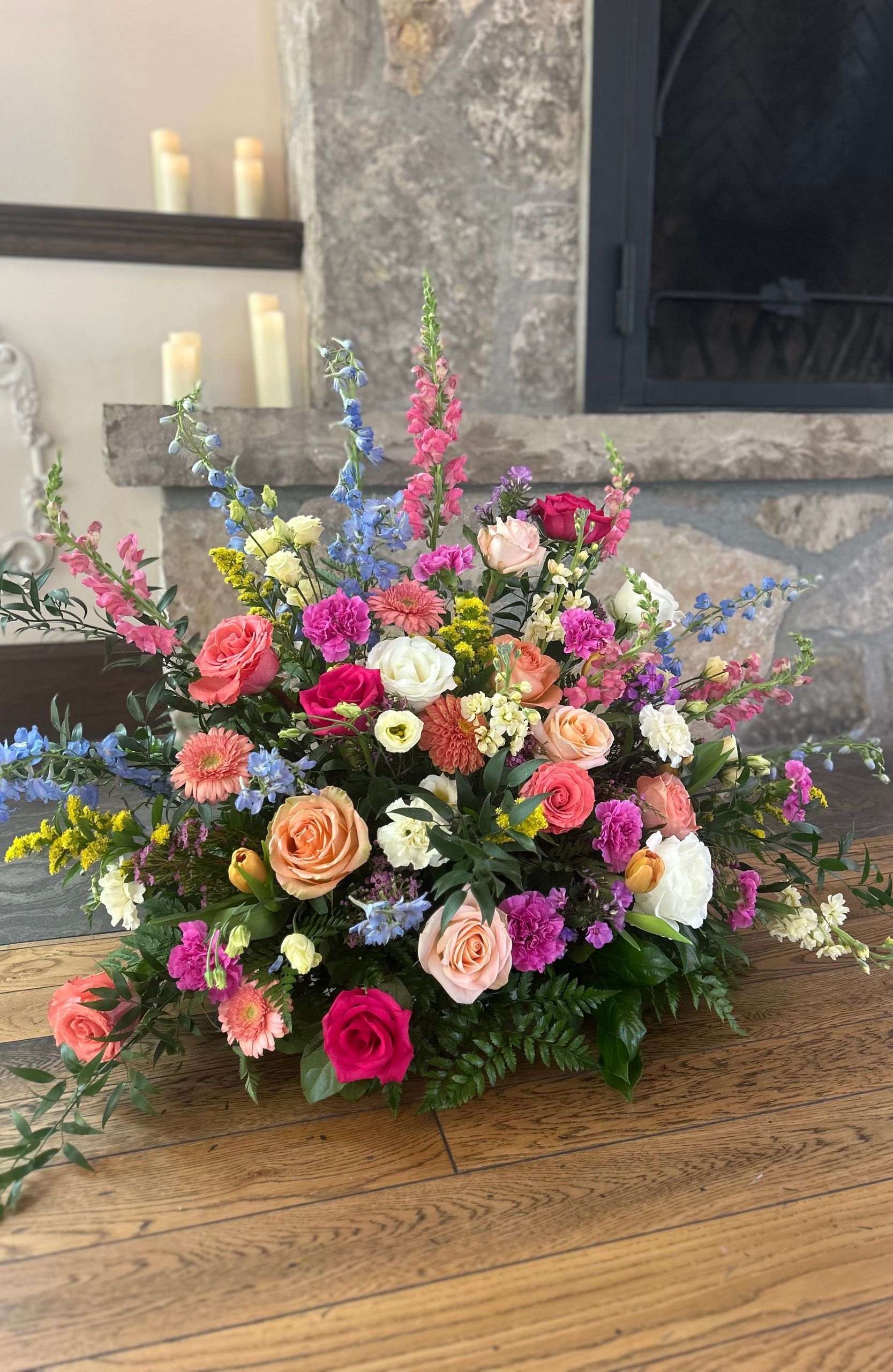 Colorful mixed flower arrangement on a wooden table beside a stone wall and window