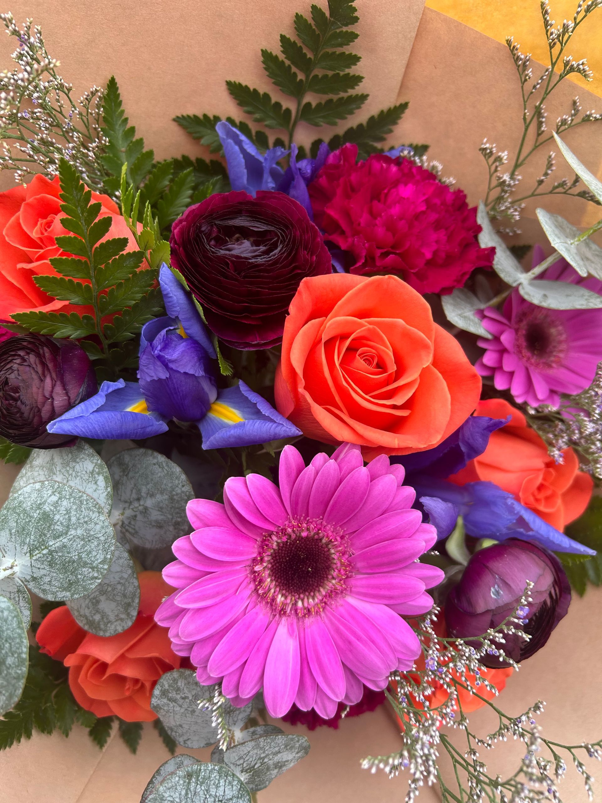 Colorful bouquet of roses, daisies, and purple flowers with green foliage on a peach background