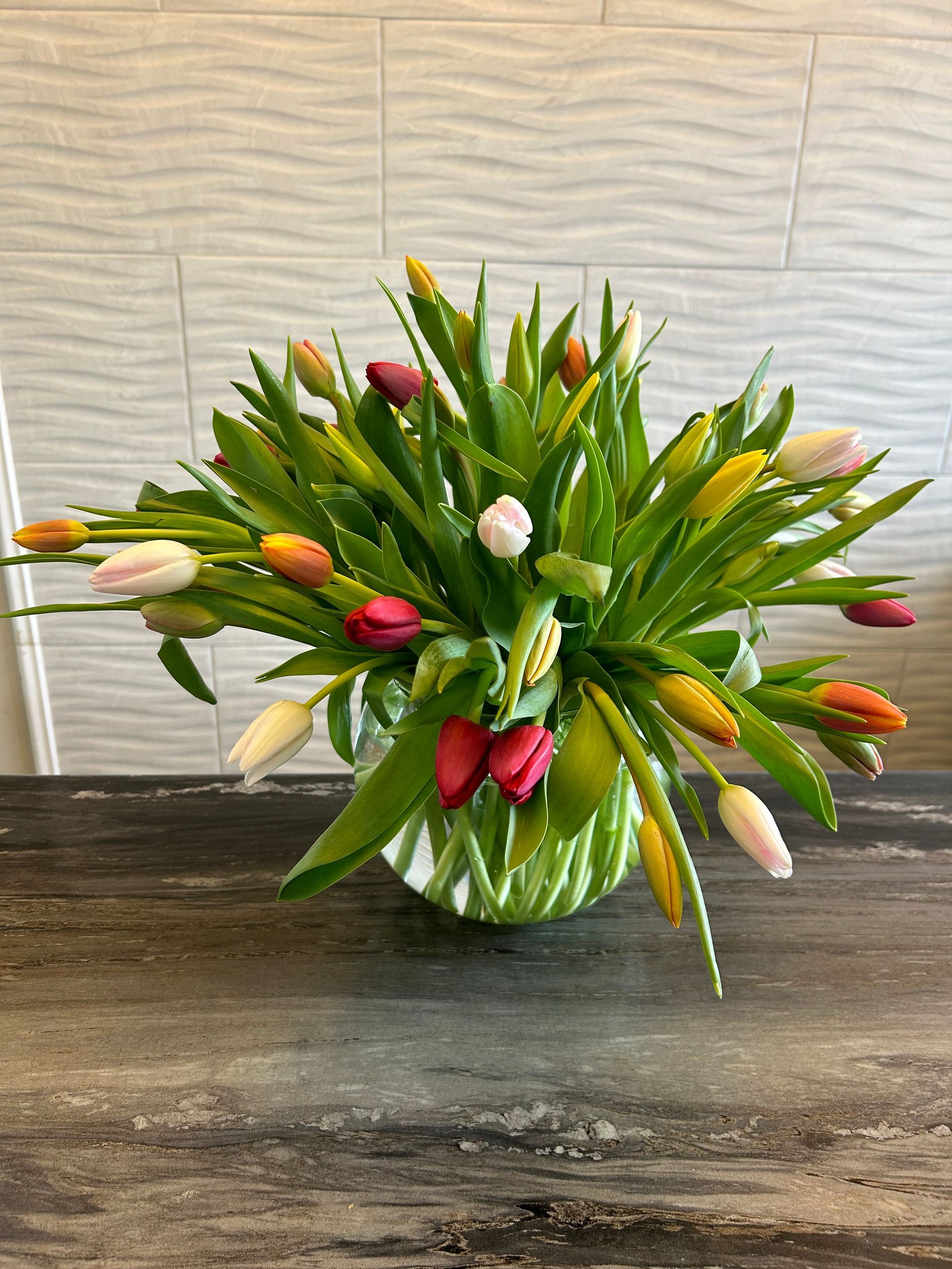 Bright bouquet of multicolored tulips in a green vase on a dark table