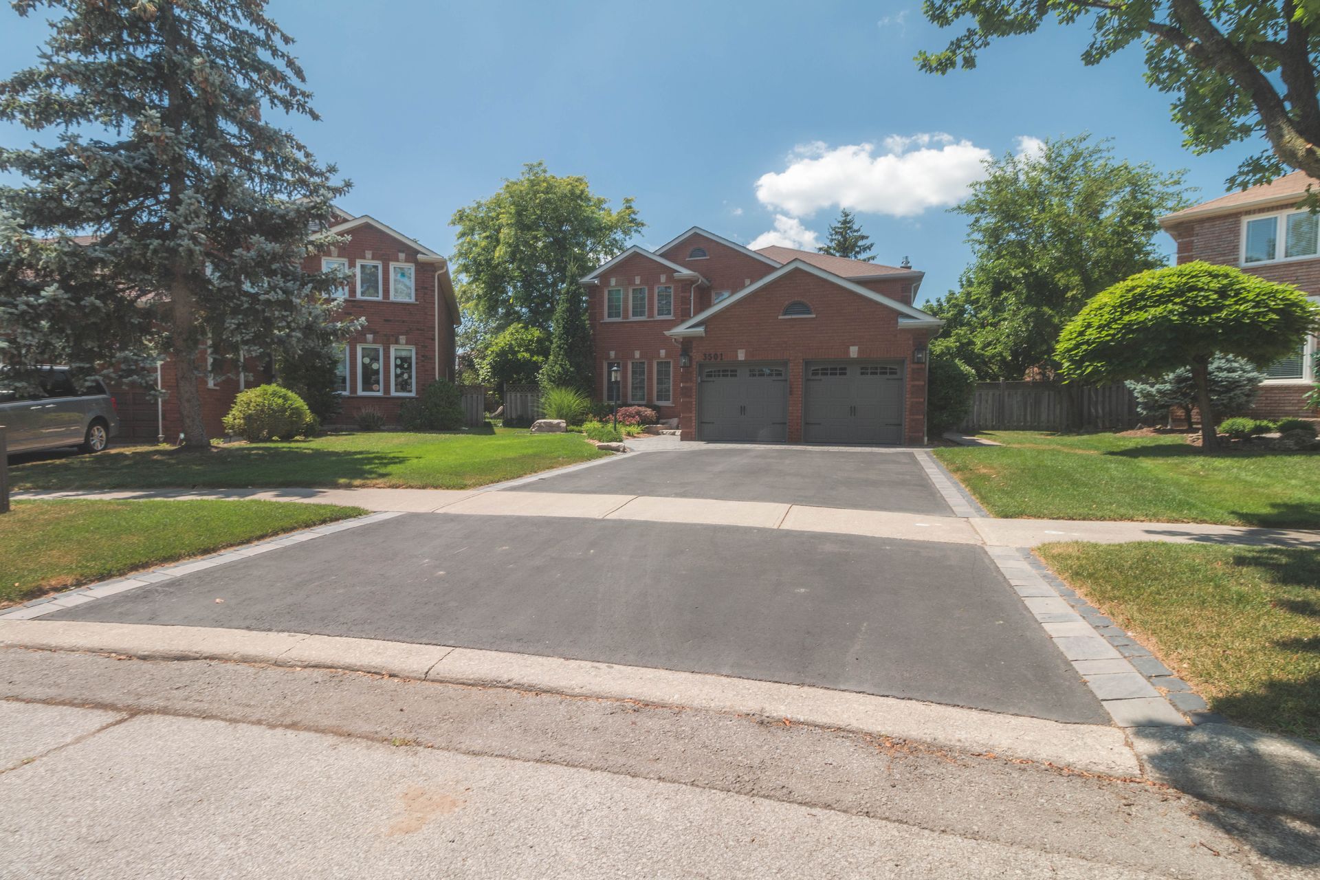 Suburban house with asphalt driveway, green lawn, and blue sky.