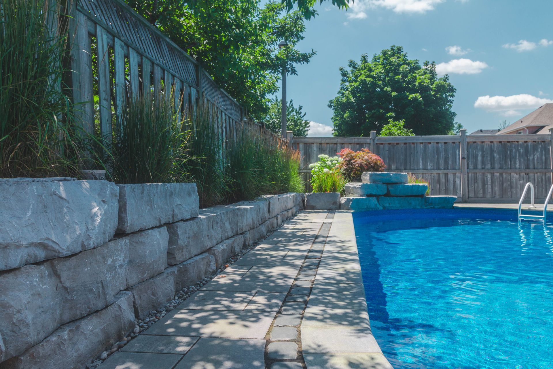 A large swimming pool is surrounded by a stone wall and a fence.