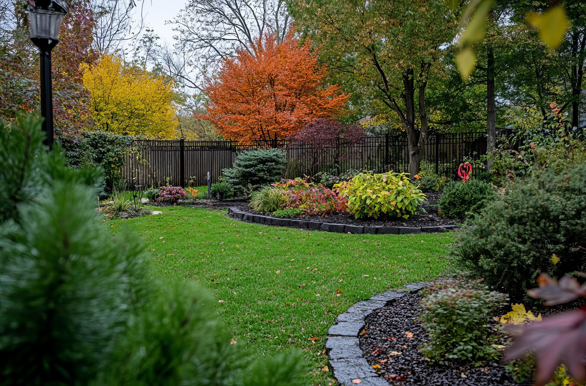 A vibrant autumn garden with colorful trees, manicured lawn, and flowerbeds.