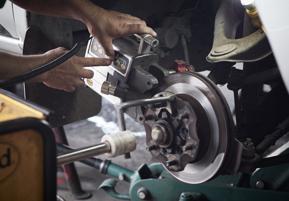 Mechanic Working on Car Brakes in a Shop, Using a Tool on the Brake Rotor — The Automotive Den in Ballina, NSW