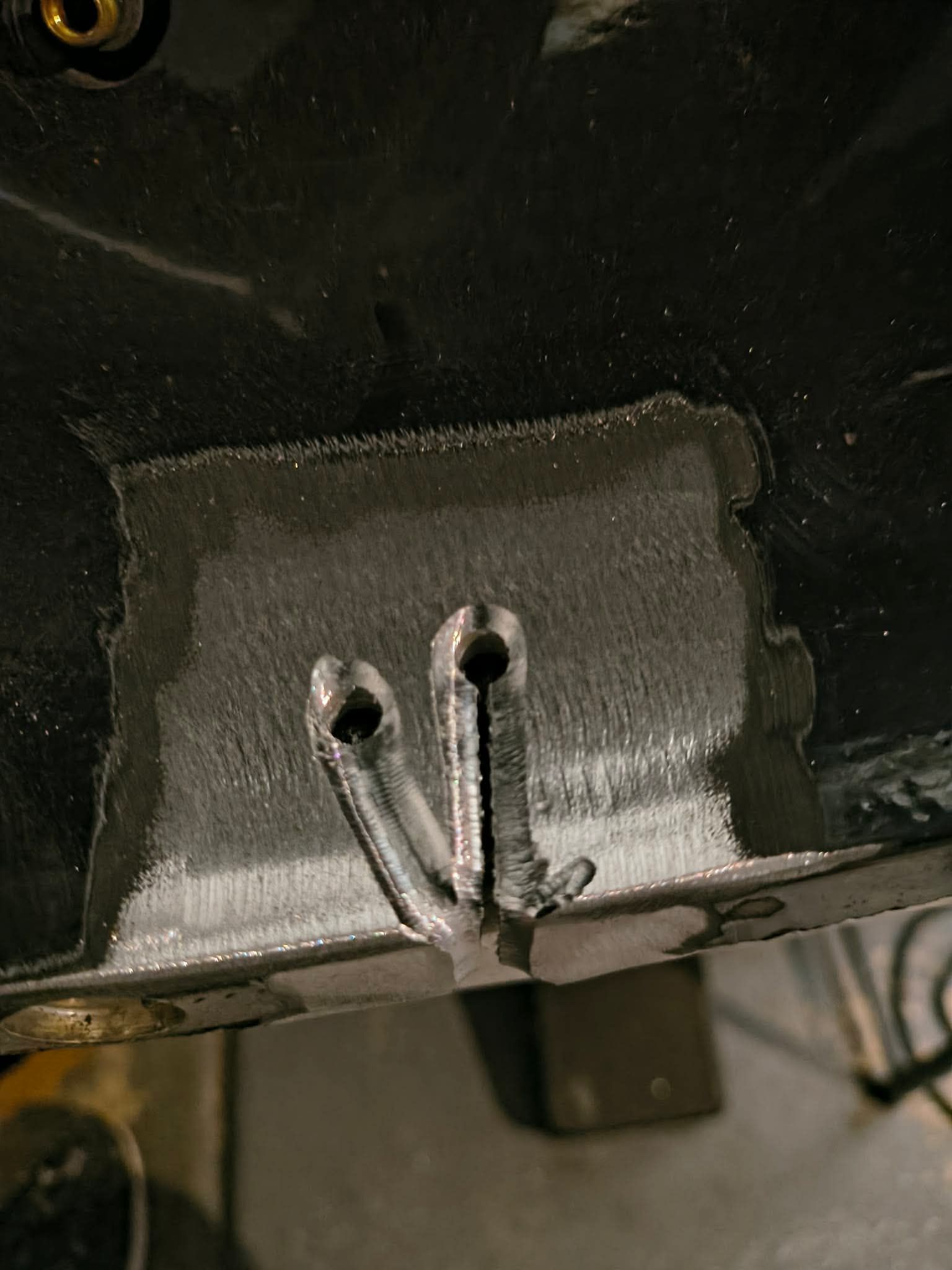 Close-up of a cracked black panel patched with gray filler and exposed screws underneath.