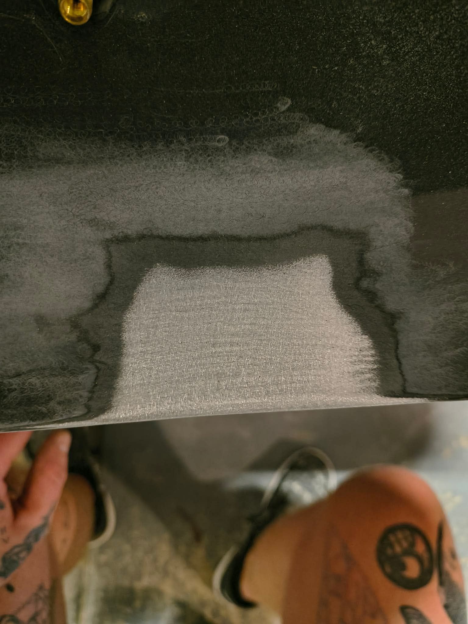 Hand holding a black panel with a cutout revealing white foam inside on a floor.