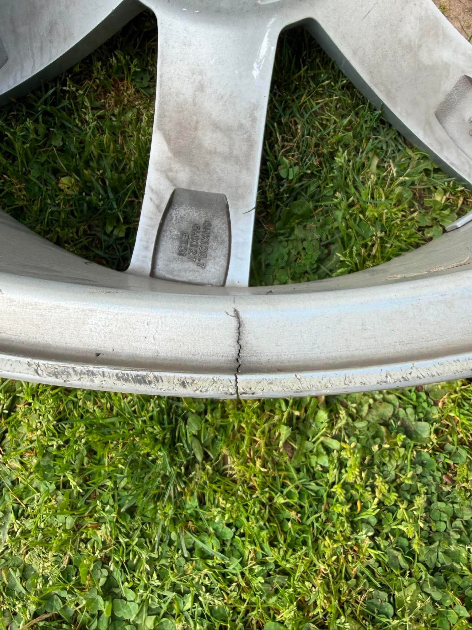 Close-up of a silver car wheel rim with a small dark patch, resting on grass